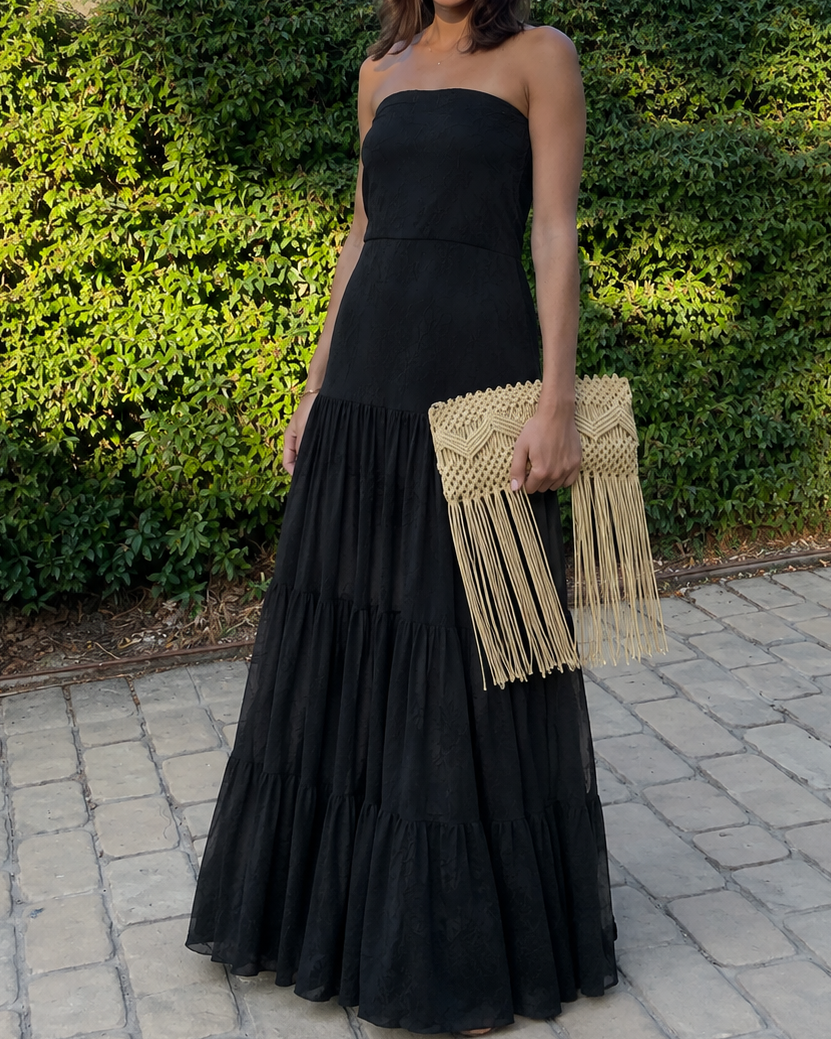 Mujer modelando un vestido largo negro strapless con mucha caída. El diseño destaca por su tejido de encaje con forro interno.