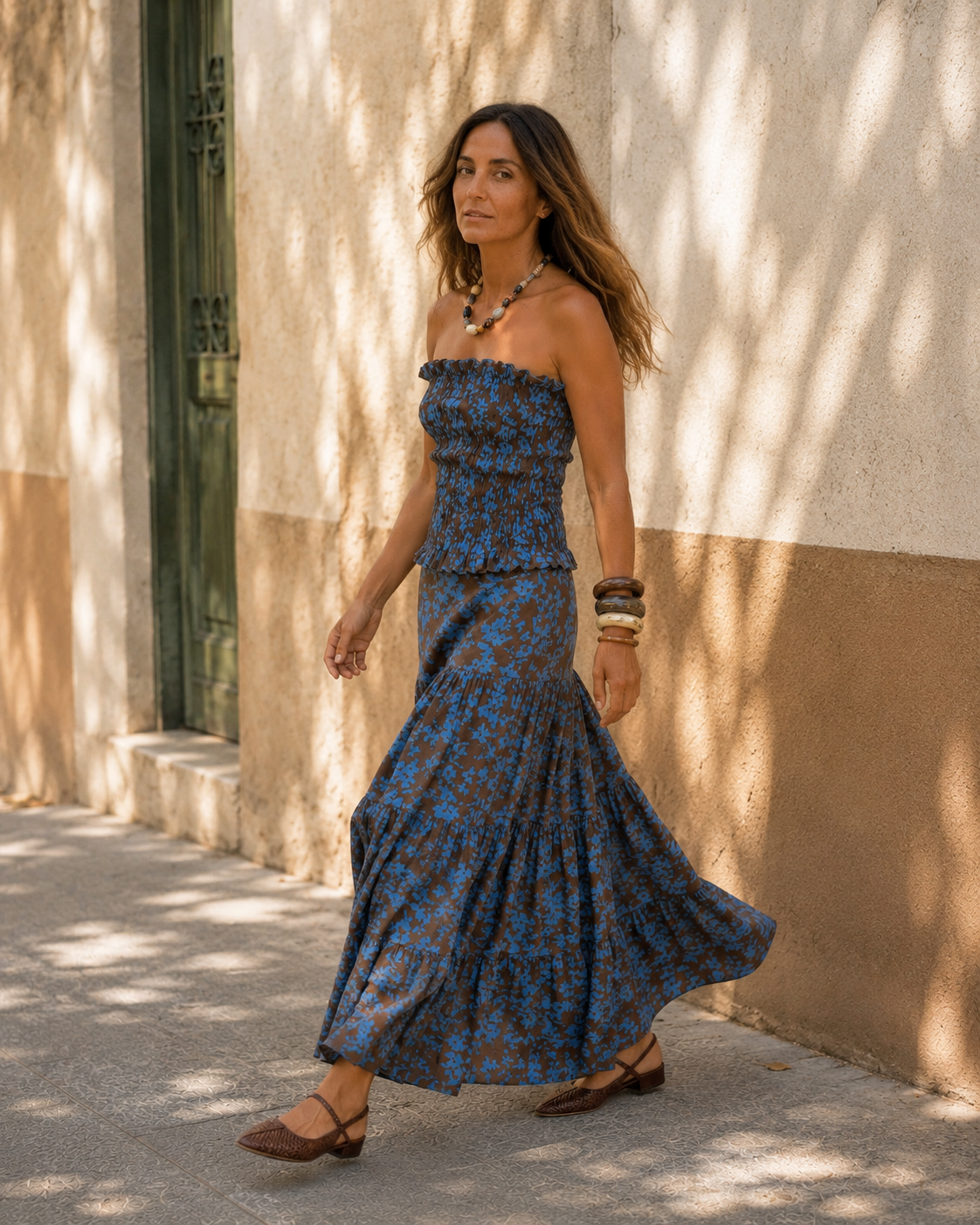 Modelo con conjunto azul y chocolate de top strapless fruncido y falda larga con volados, caminando en una locación exterior de estilo mediterráneo.
