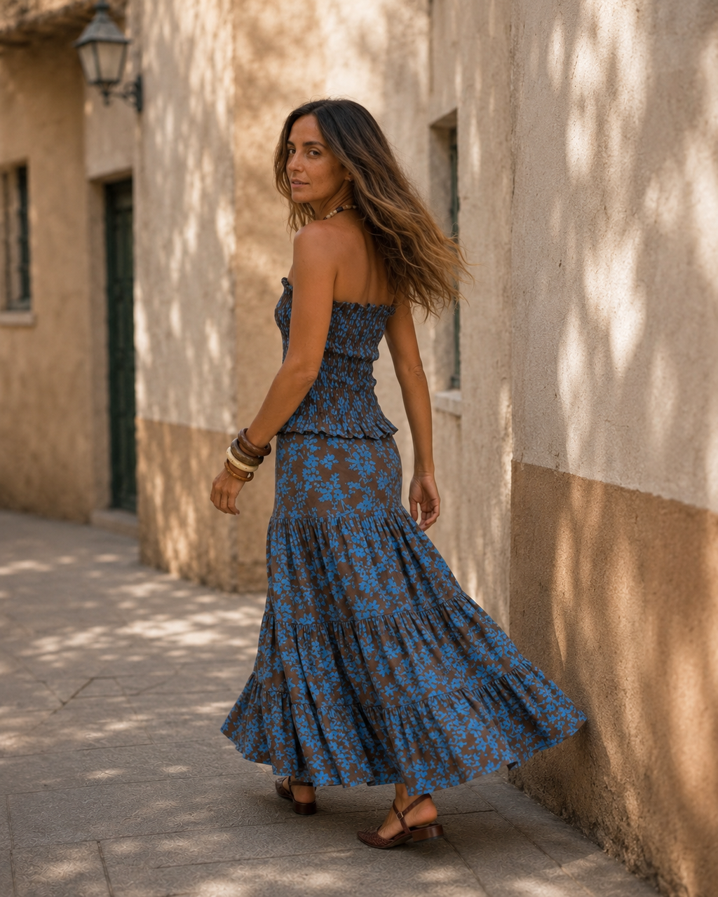 Modelo con conjunto azul y chocolate de top strapless fruncido y falda larga con volados, caminando en una locación exterior de estilo mediterráneo.