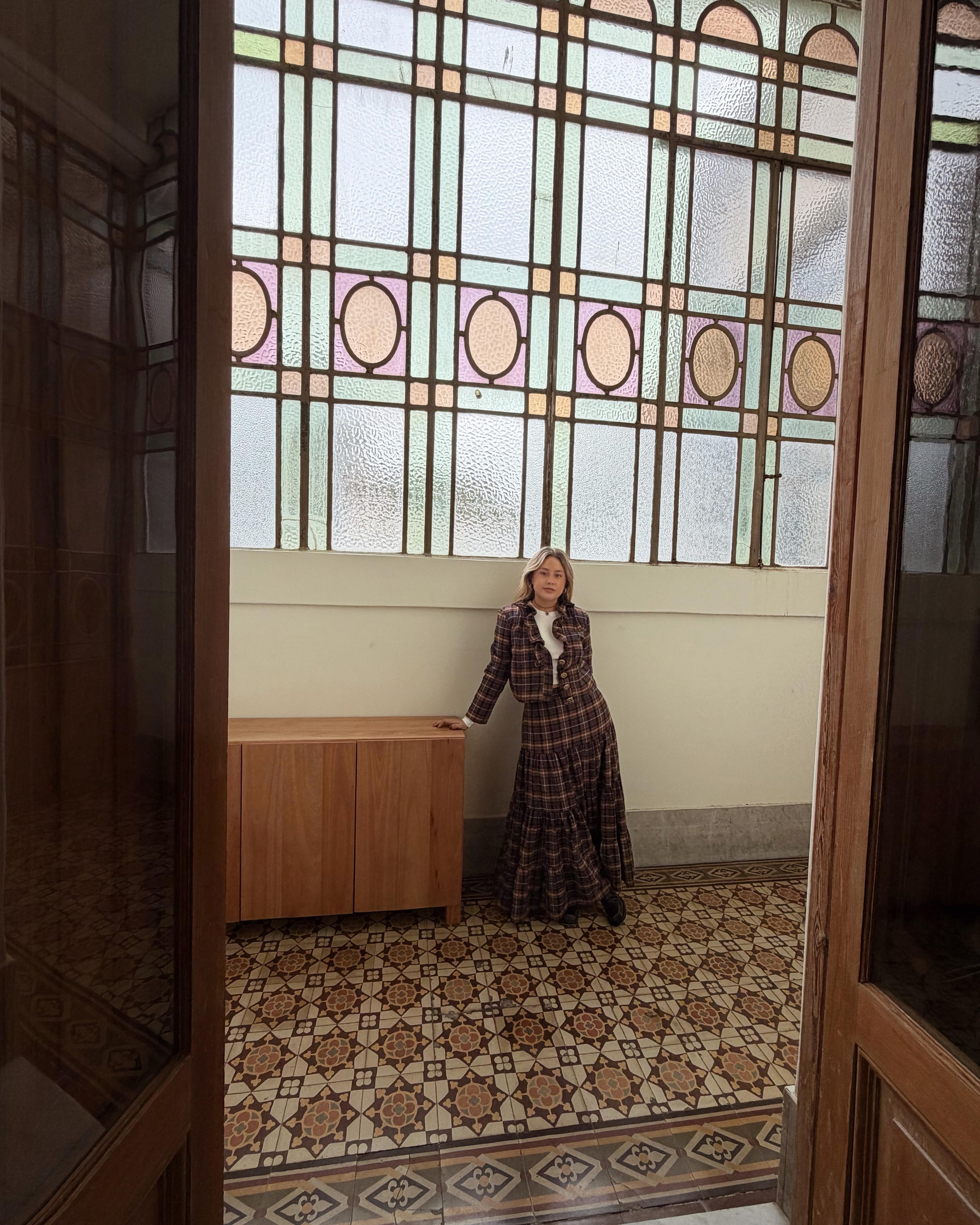 Conjunto escocés de blazer entallado y falda larga, usado por una modelo en un espacio interior de estilo antiguo con vitrales y piso ornamental.