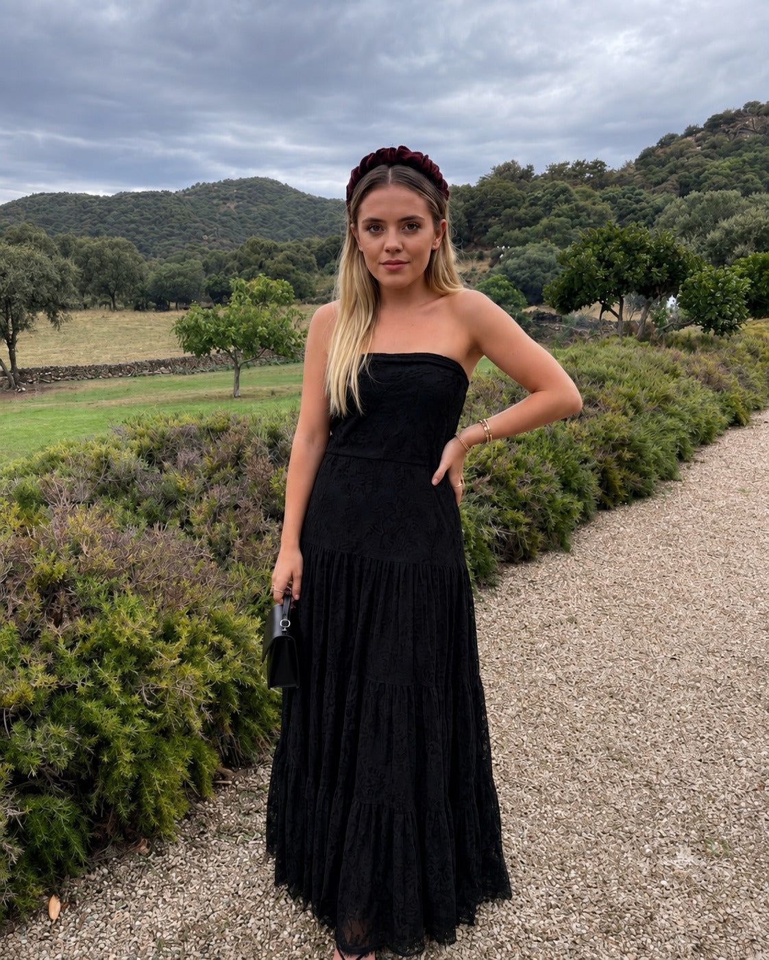 Mujer modelando un vestido largo negro strapless con mucha caída. El diseño destaca por su tejido de encaje con forro interno.