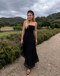 Mujer modelando un vestido largo negro strapless con mucha caída. El diseño destaca por su tejido de encaje con forro interno.